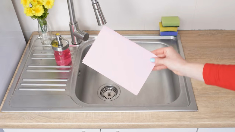 Woman's hand holding a pink piece of paper above a sink