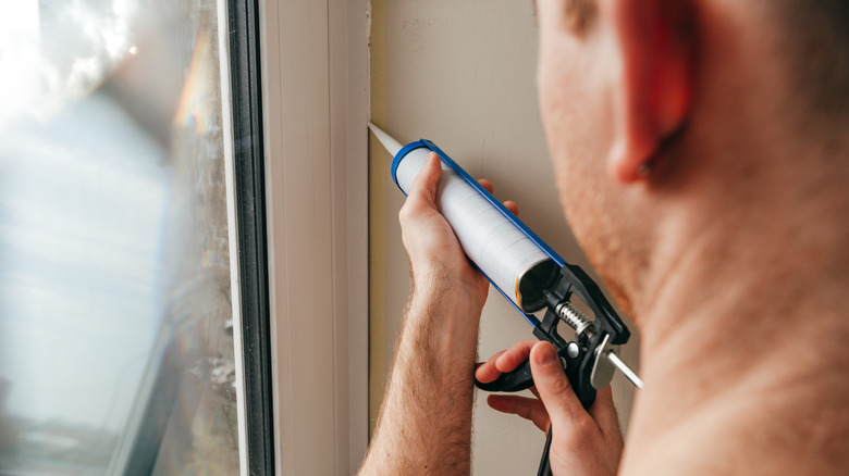 Man seals crack near the window with a caulk gun