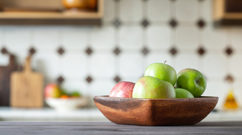 Wooden bowl holding green and red apples in a rustic kitchen