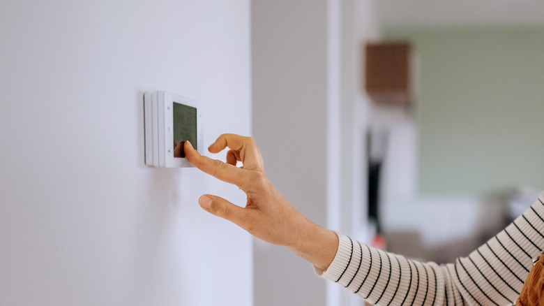 Woman in striped shirt sets thermostat temperature