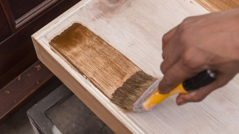 A carpenter applying varnish to a cabinet drawer with a paintbrush