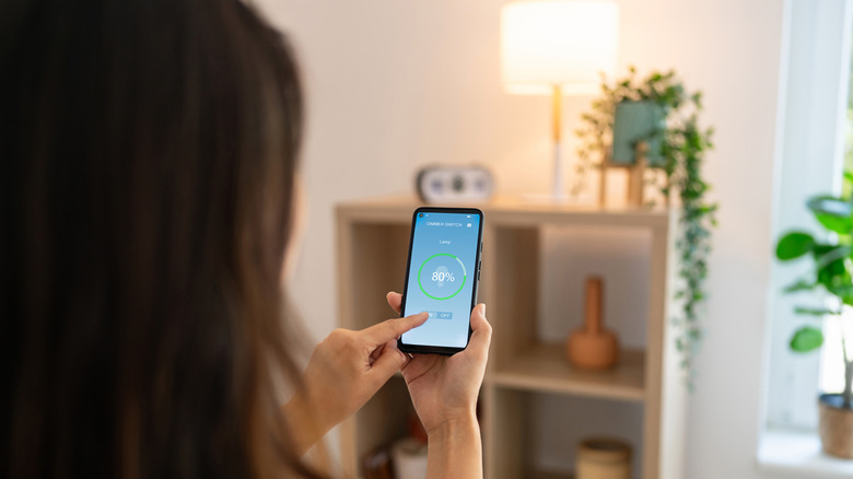 Woman using a smart phone app to control lighting with a lamp in the background