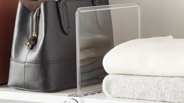 A shelf with shoes and clothing divided with a clear shelf divider