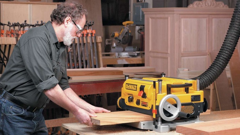 Man feeding a piece of wood into the DW735X 2-Speed Bench Planer in a shop
