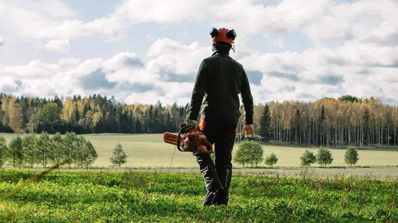 Man carrying Husqvarna chainsaw in open field