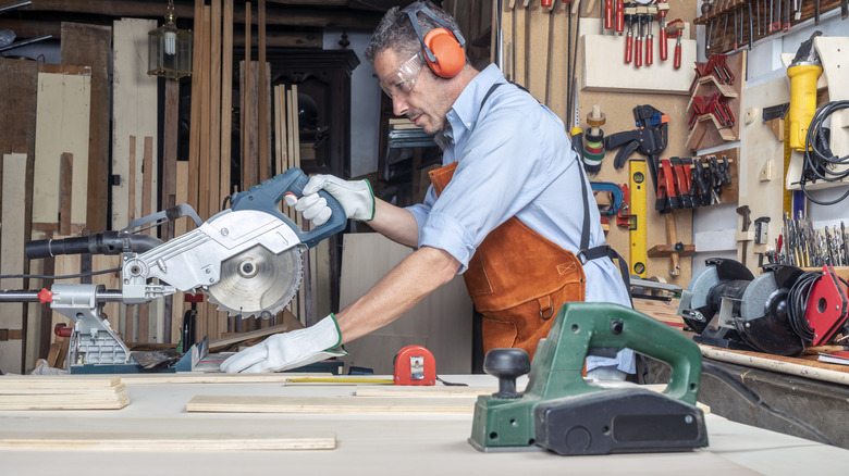 Man using a saw to cut wood in a workshop filled with tools