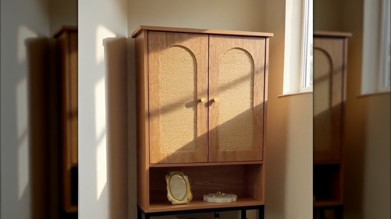 A picture frame is placed on an over-the-toilet shelf with doors