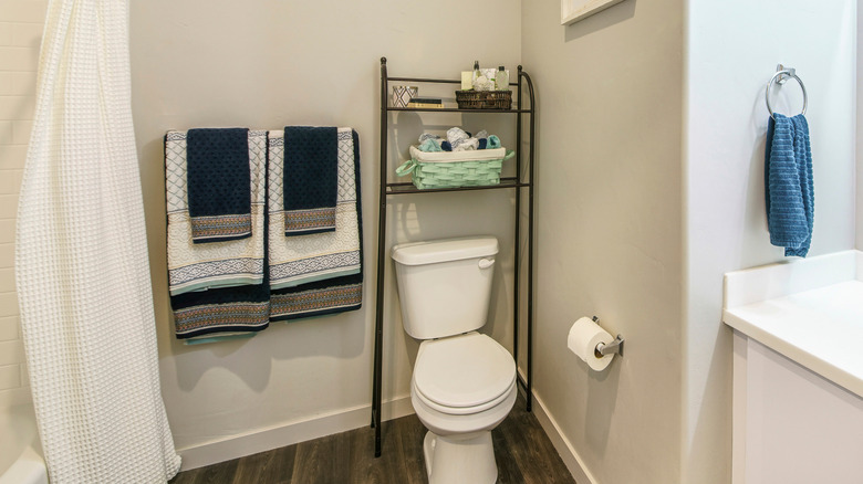 A black wire over-the-toilet shelf in a neat bathroom with blue towels and white walls