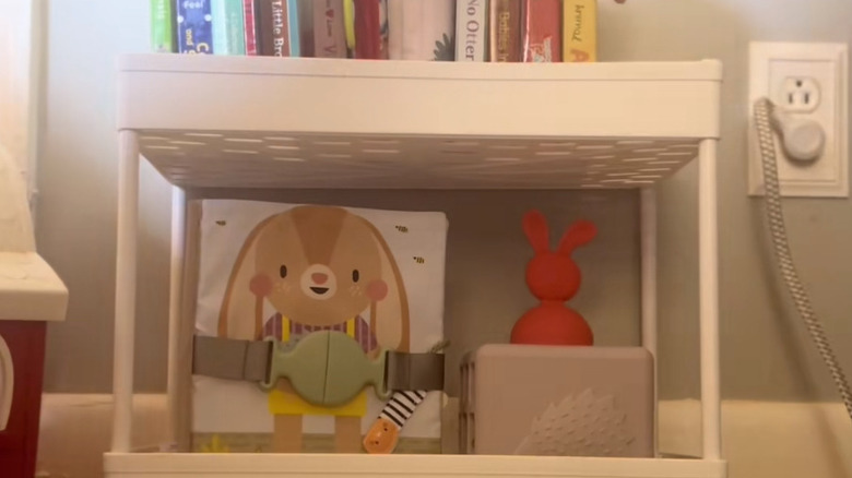 Board books and toys are placed on a white over-the-toilet shelf