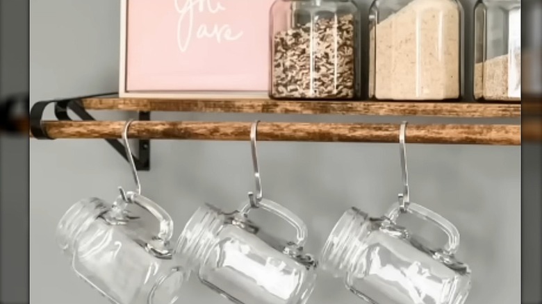 Wooden stained shelf with black brackets made into open shelving holding mugs on S-hooks