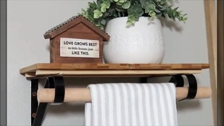 Wooden shelf made with cutting boards and plant brackets holding a grey and white striped towel with a dowel