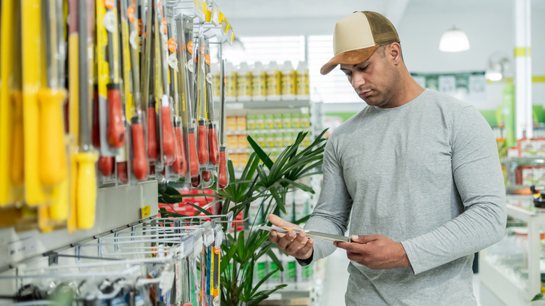 Man in two-tone trucker hat shopping for gardening tools in a store