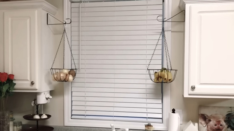 Two hanging baskets hung above a sink in a white kitchen via black plant brackets