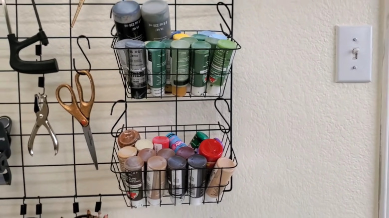 Wire baskets containing paint hung on rack using black plant hooks