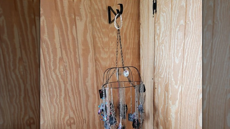 Wall-mounted black plant bracket holding a wire basket strung with necklaces