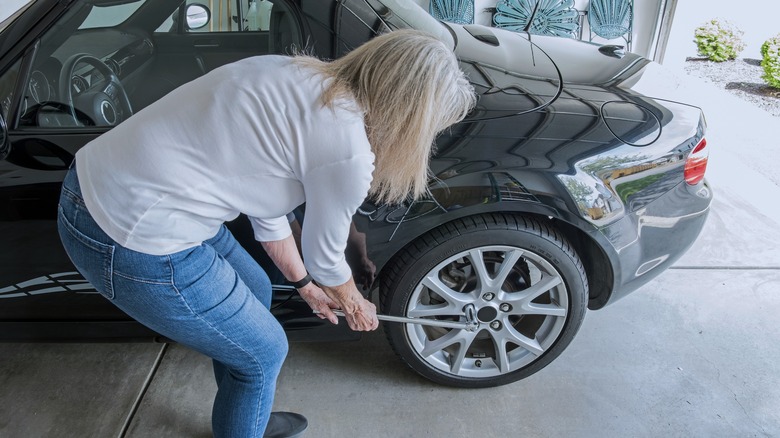 A woman using a breaker bar on car wheel nuts