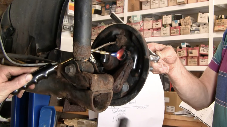 Close-up of men using a propane torch to heat a rusted bolt