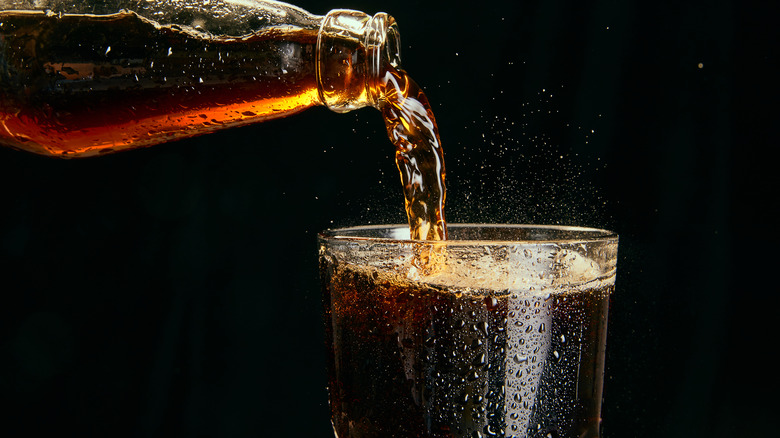 A glass of cola being poured from a glass bottle