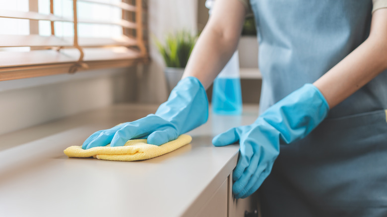 A person wearing blue gloves and cleaning a countertop