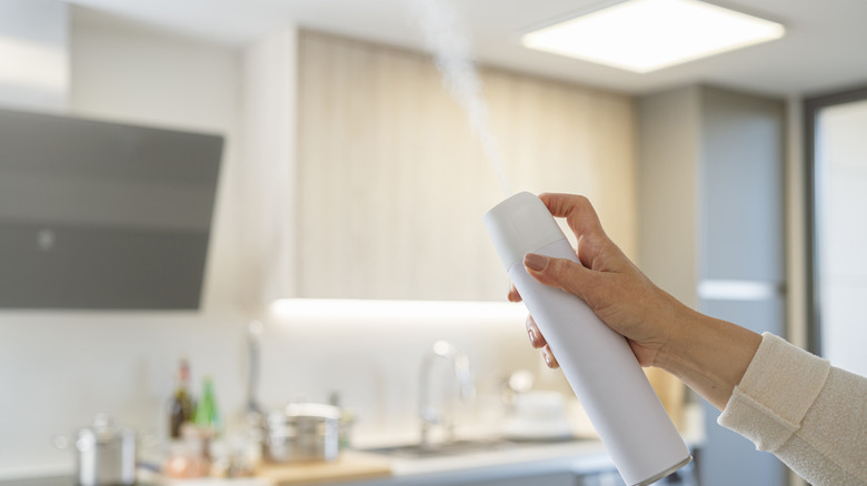 Someone spraying a can of air freshener in a kitchen