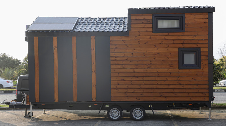 A dark wood tiny house on wheels in a parking lot