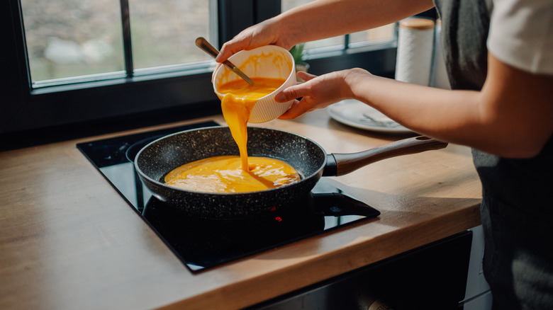 Someone making eggs in a frying pan on a small two burner stovetop