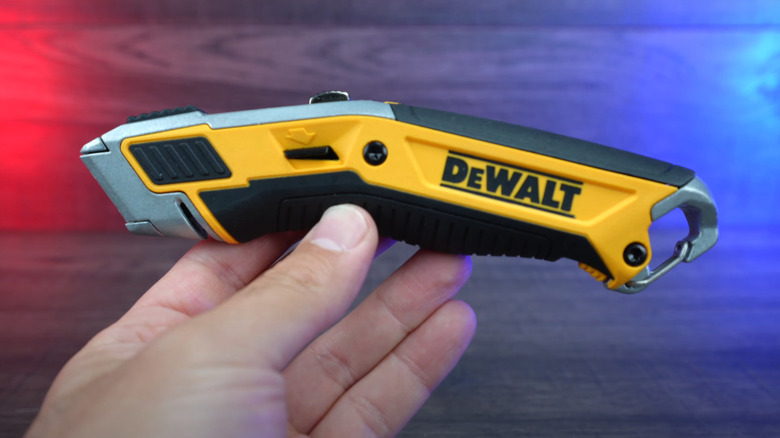 Hand holding popular DeWalt utility knife over wood surface