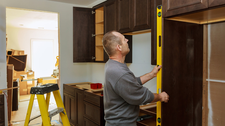 Man leveling kitchen cabinet and fridge space for full kitchen remodel