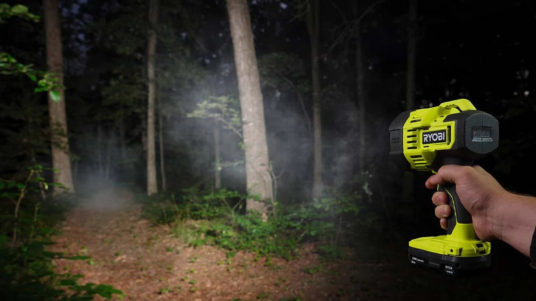 A person shining Ryobi's 18V One+ Cordless LED Spotlight into a dark wooded area
