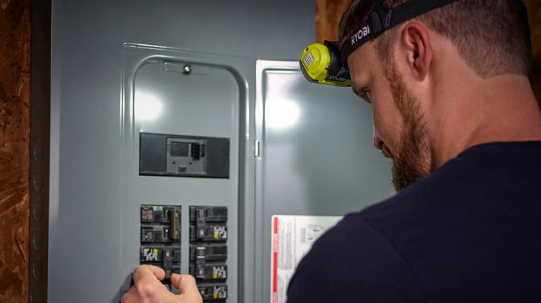 A person working on an electrical breaker board with Ryobi's USB Lithium Magnetic LED Headlamp Kit with 2Ah Battery and Charging Cord