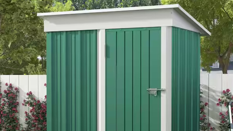 A green patiowell shed against a white fence.
