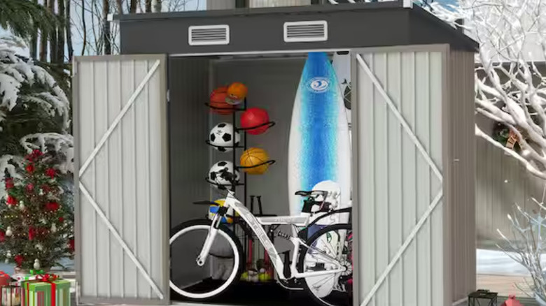 A large bike and surf board stored in the double door shed.