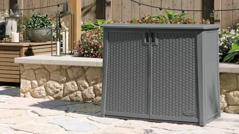 The gray mini Suncast storage cabinet on a stone patio.