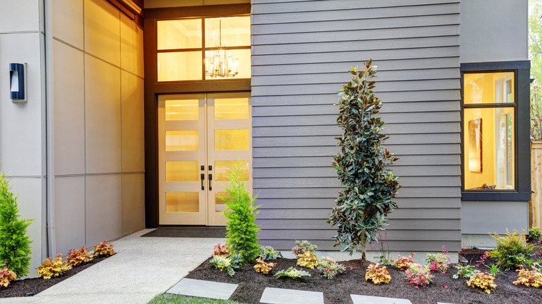 The front of a home with a modern double front door, windows, and a garden.