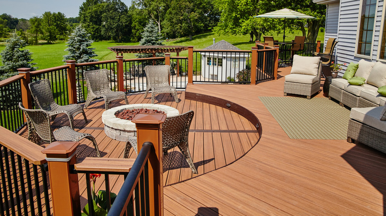 An outdoor deck made of wood with patio furniture overlooking a manicured, tree-filled backyard.