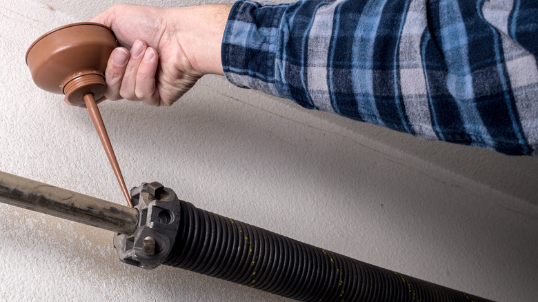 Person wearing a blue plaid shirt applies oil to the garage door spring