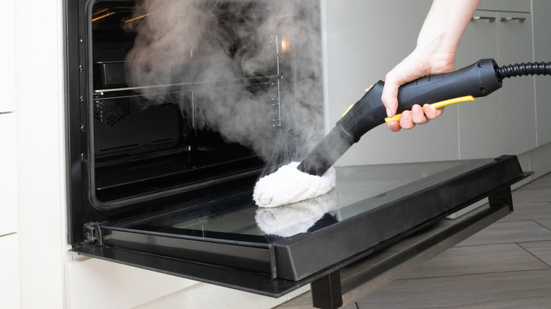 Close-up of a person using a steam cleaner on an oven