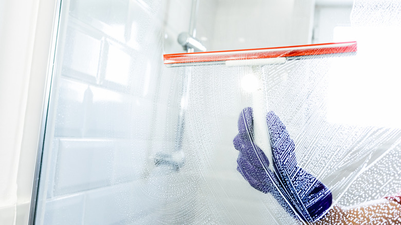 Hand with glove cleaning a shower screen with a squeegee