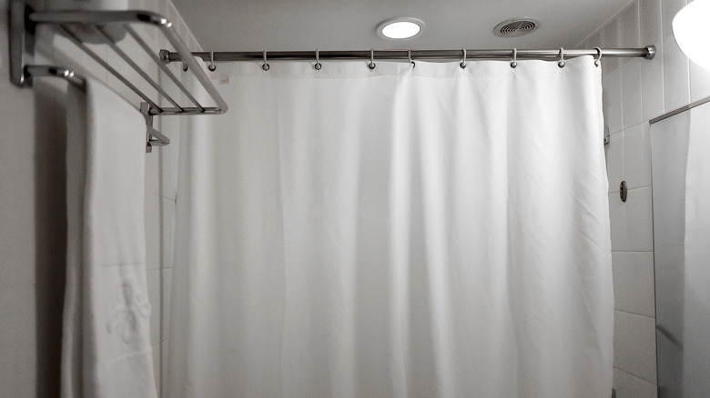 White shower curtain hanging from a shower curtain rod in a bathroom