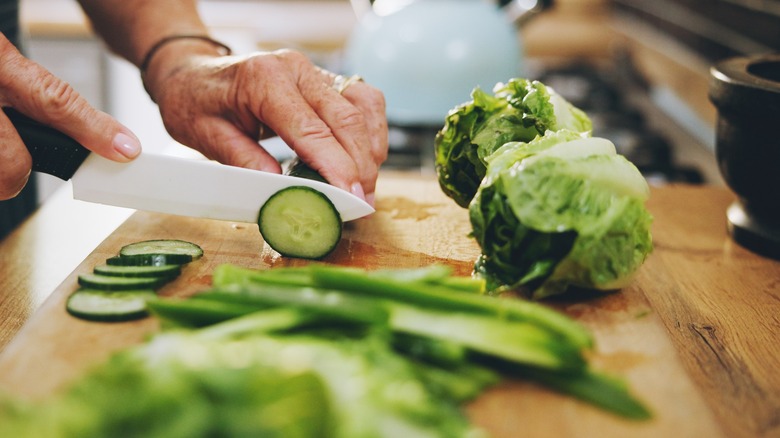 Person using a knife to cut vegetables on a wood cutting board