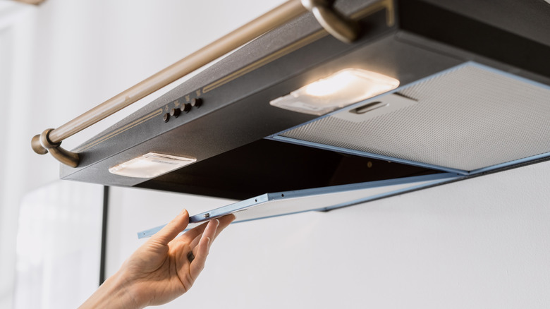 Hand removing a range hood filter for cleaning