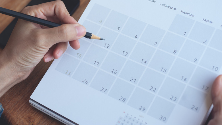 A person holding a pencil pauses before writing on a calendar.