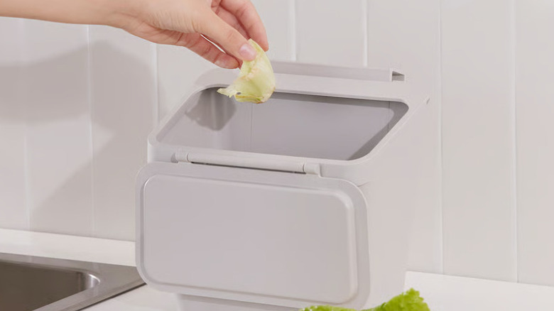 A hand is seen disposing of some scraps in an Ikea countertop wastebasket