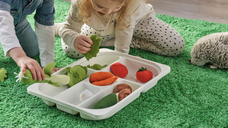 An IKEA  TROFAST storage tray with multiple compartments being used by children sitting on a bright green rug