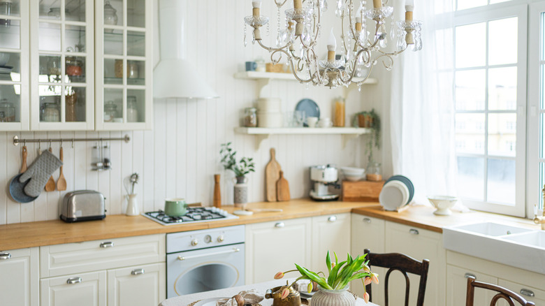 A bright off-whtie kitchen with glass windows, glass-fronted cabinets, and a glass chandelier