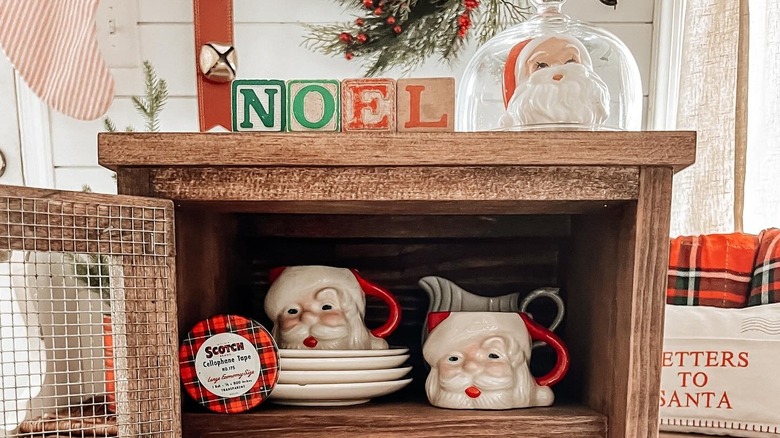 Vintage Christmas decor, including Santa-shaped mugs, in a cabinet.