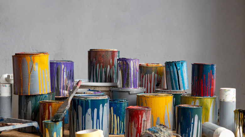 A large pile of dripping used paint cans in different colors