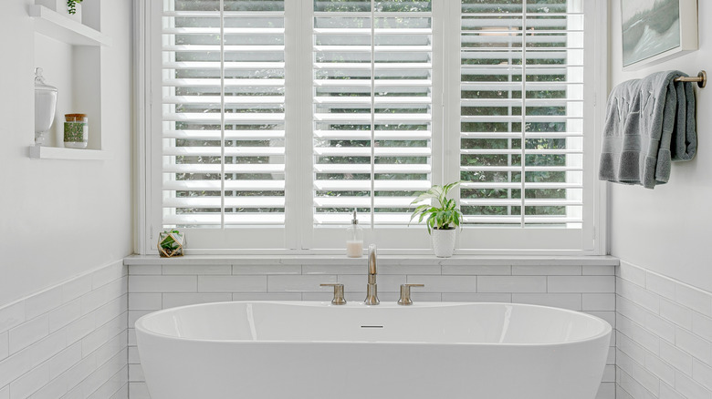 A bathtub underneath plantation shutters.