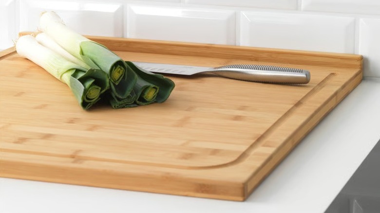 Green onions and a knife on a cutting board placed on a white counter