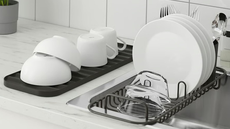 A loaded dish rack over a sink near a drain board holding cups and bowls